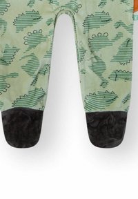 Pantalones verdes para bebé con cubiertas de pies oscuras que presentan un patrón de dinosaurios a rayas y botones a presión a lo largo de la costura interior.