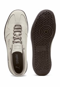 Tenisi din suede gri deschis, cu vârful rotunjit, șireturi plate și o talpă exterioară din cauciuc maro texturat, cu modele circulare.