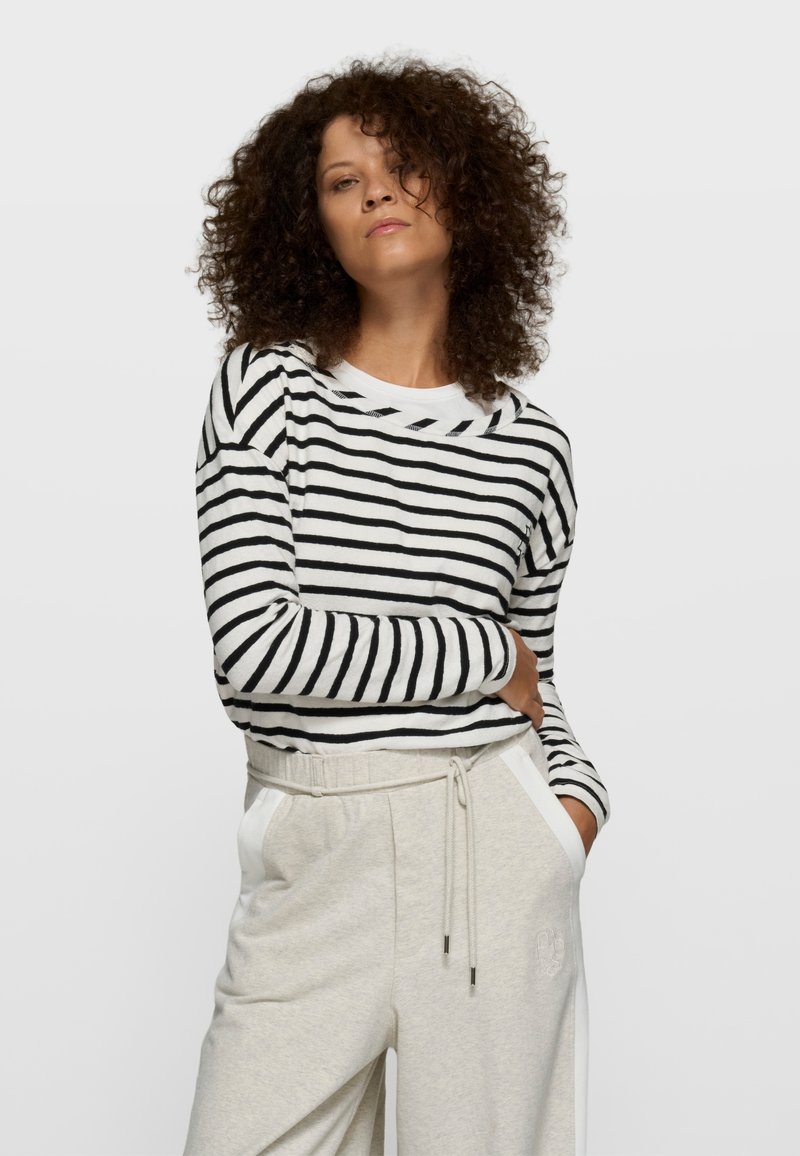 Chemise à manches longues rayée en coton noir et blanc, col rond ; associée à un pantalon gris clair avec poches latérales et taille élastique.