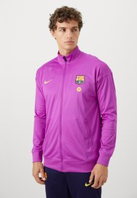 Paarse zip-up jas van gladde stof met lange mouwen, voorzien van een teamlogo op de borst en een zijzak.