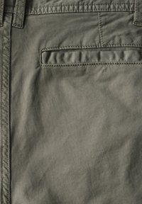 Olivově zelené kalhoty s hladkou strukturou, s zadní kapsou a prošívanými detaily podél pasu a švů.