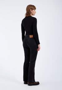Jeans in denim neri con vestibilità dritta, vita alta e tasche posteriori discrete, abbinati a un top aderente a maniche lunghe nero.