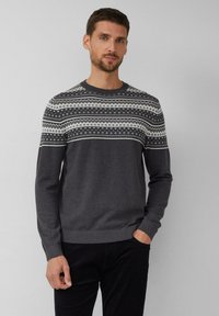 Homme avec des cheveux courts et foncés et une barbe, portant un pull en gris foncé avec un motif nordique en blanc et gris clair sur la poitrine et les épaules.