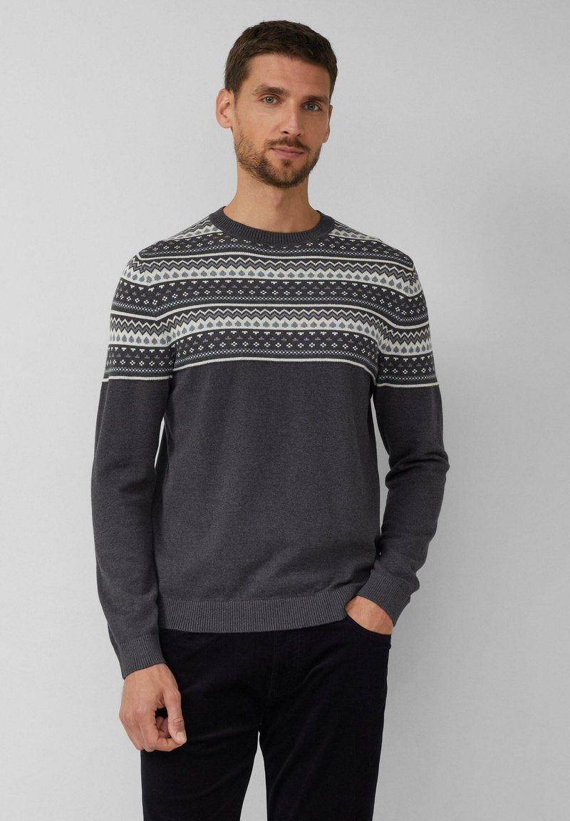 Homme avec des cheveux courts et foncés et une barbe, portant un pull en gris foncé avec un motif nordique en blanc et gris clair sur la poitrine et les épaules.