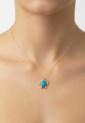 Aranylánc nyaklánc türkiz teknős medállal, amelynek fejét, uszonyait és farkát gyémántok díszítik, egy nő nyakán.