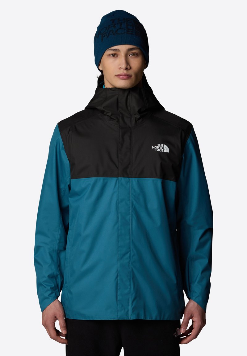 Teal-värinen vedenpitävä takki mustilla olkapäillä, säädettävä huppu ja vetoketjullinen etuosa. The North Face -logo vasemmassa rinnassa. Pehmeä neulotumpra.