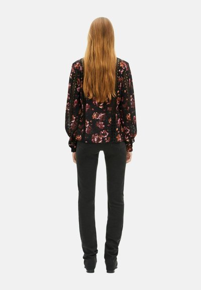 Blusa nera a fiori con maniche ampie, aderente in vita. Abbinata a pantaloni neri slim-fit. Capelli lunghi e lisci.