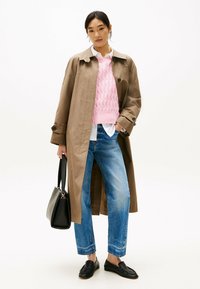 Abrigo de trench color marrón claro sobre un suéter de punto de cable rosa, camisa blanca, jeans azules y mocasines negros. Un bolso negro completa el look.