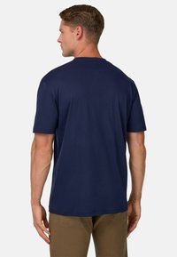 Námořnická modrá tričko s krátkým rukávem, kulatý výstřih, hladká textura, uvolněný střih, jednobarevné bez vzorů, nošeno s světle hnědými kalhotami.