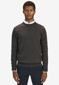 Mörkgrå crewneck-tröja i mjukt stickat tyg, med långa ärmar och ribbade muddar, lager på lager över en vit skjorta med krage.