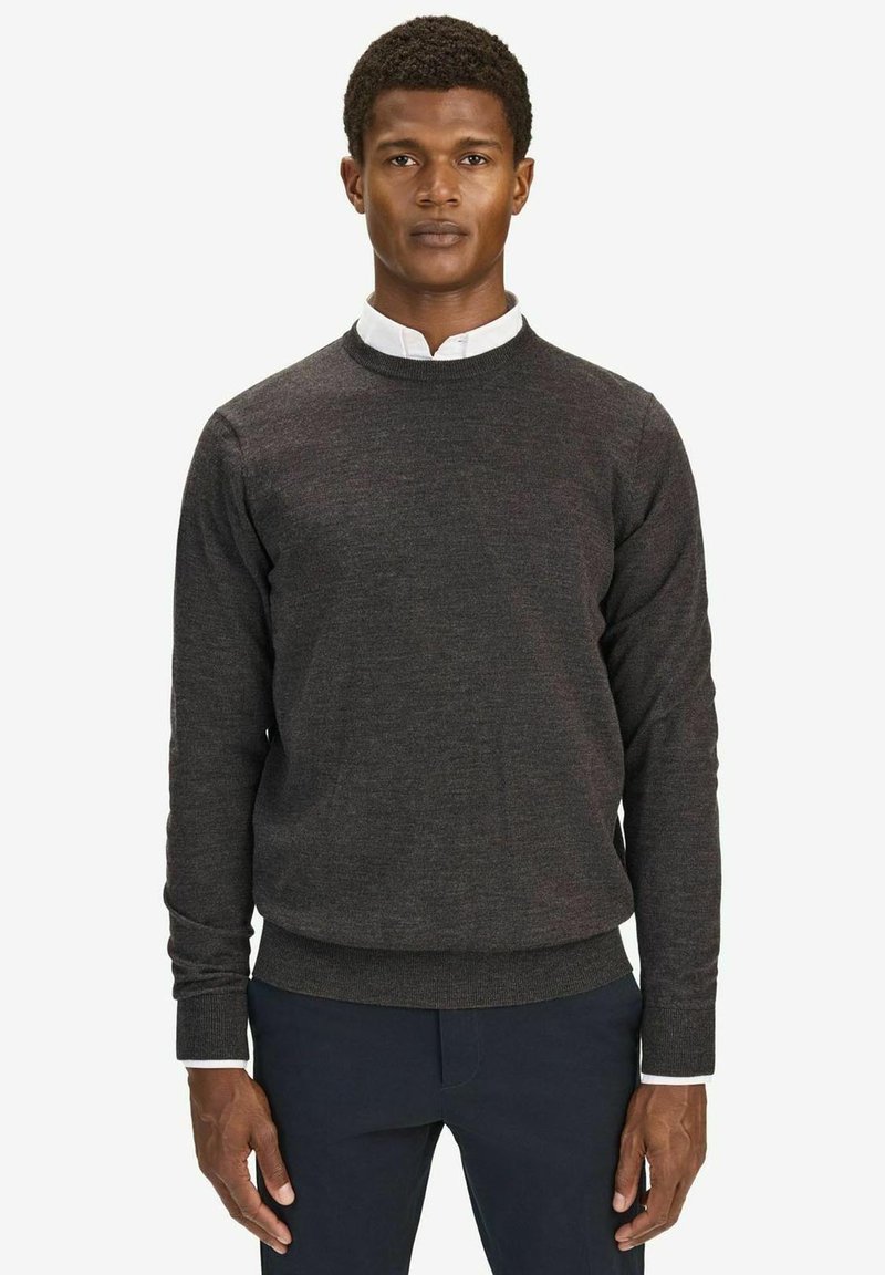 Mörkgrå crewneck-tröja i mjukt stickat tyg, med långa ärmar och ribbade muddar, lager på lager över en vit skjorta med krage.