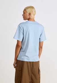 Lichtblauw katoenen T-shirt met korte mouwen en een ronde hals, gedragen met bruine cargoshort met zijzakken en een patchdetail.