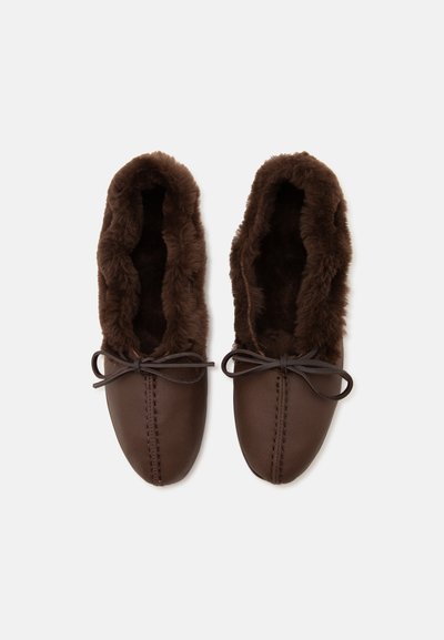 Paire de chaussons mocassins marron avec doublure en fourrure douce et nœuds en cuir noués sur un fond clair uni.