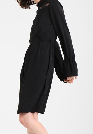Zwarte jurk met lange, klokvormige mouwen en een getextureerde kraag. Gemaakt van een lichtgewicht materiaal, kniehoogte, met een losse pasvorm.
