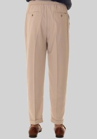 Pantaloni beige su misura con vita elastica, con pieghe davanti e tasche posteriori, mostrati con polsini arrotolati e scarpe marroni texture.