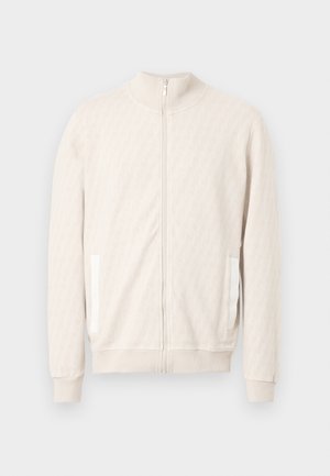 Šviesiai smėlio spalvos užsegama su užtrauktuku striukė su imitacine aukšta apykakle, tekstūruotu deimanto raštu, ribinėmis rankogalių detalėmis ir dviem šoninėmis kišenėmis baltomis akcentais.