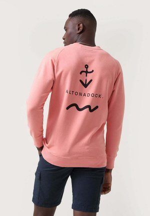 Sudadera rosa con un diseño de ancla negra y olas en la parte posterior, hecha de material suave con puños y dobladillo acanalados.
