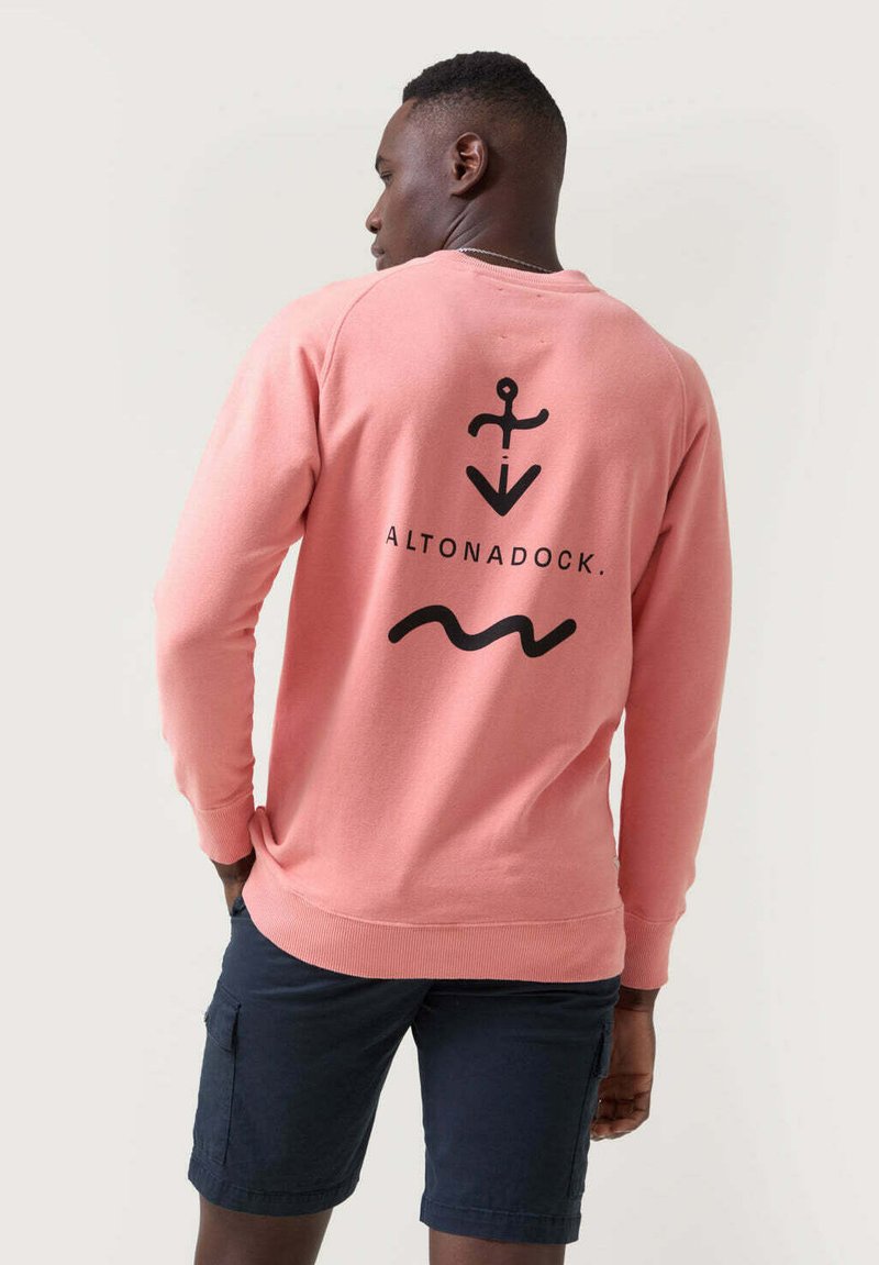 Sudadera rosa con un diseño de ancla negra y olas en la parte posterior, hecha de material suave con puños y dobladillo acanalados.