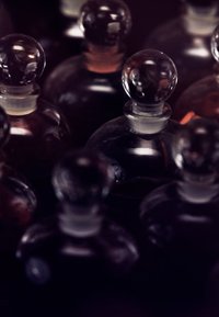 Gruppo di bottiglie di profumo in vetro con tappo rotondo. Diverse tonalità scure, alcune contengono liquido visibile. Texture liscia, forme eleganti.