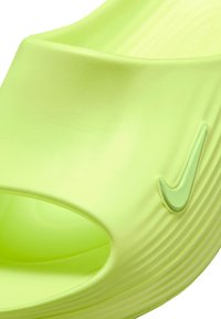 Κοντινό πλάνο ενός lime πράσινου σκαρπίνιου Nike, που δείχνει το υφασμάτινο λουράκι, το ανοιχτό πλάι και το ανάγλυφο λογότυπο Nike στη εξωτερική άκρη.