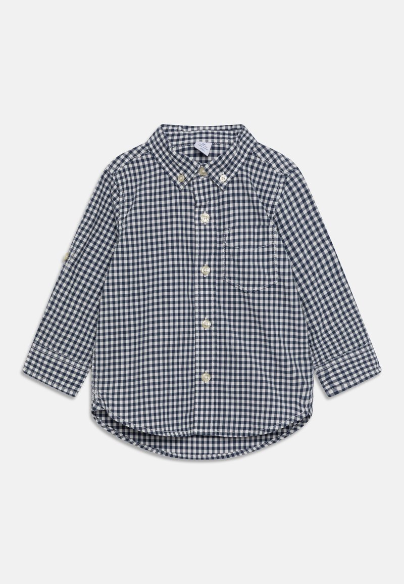 Chemise à manches longues à carreaux bleu marine et blanc, avec une poche avant et un col boutonné, posée à plat sur un fond clair.