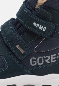Marineblaue Schuhe, die aus einer Kombination von Wildleder und Textilmaterialien bestehen, mit einem Klettverschluss und grauer "GORE-TEX"-Markierung. Weiße Gummisohle.