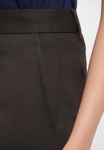 Καφέ �ραμμένο παντελόνι με ομαλή, υφασμάτινη υφή. Διαθέτει ελαφρώς κωνικό σχήμα, πλαϊνές τσέπες και διακριτικές κόκκινες ραφές ως διακοσμητικά στοιχεία.