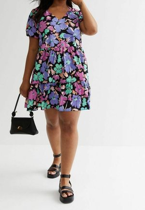 Sukienka w kwiaty na czarnym tle, z fioletowymi, zielonymi i różowymi kwiatami, krótkimi bufiastymi rękawami oraz warstwowym krojem. Czarna torebka i sandały na platformie.