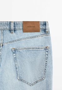 Light blue denim jeans feature a brown leather label with the text "Massimo Dutti" and two back pockets with subtle stitching details.