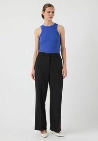 Blauwe geribbelde tanktop en hooggewaisted zwarte wijdlopende broeken. De outfit wordt compleet gemaakt met puntige witte hakken.