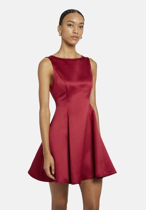 Femme portant une robe A-line sans manches en satin rouge, avec un corsage ajusté et une jupe évasée, se tenant devant un fond blanc.