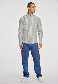 Stribet langærmet skjorte i grå og hvid, parret med blå lige ben jeans og hvide sneakers. Knap-ned krave, struktureret stof.