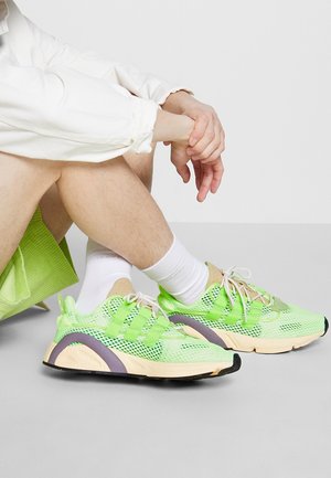 Sneakers a rete verde neon con accenti beige, superfici testurizzate, tre cinghie e una suola leggera con dettagli viola.