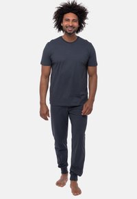 Czarny, szary t-shirt z krótkimi rękawami w połączeniu z dopasowanymi spodniami dresowymi. Spodnie mają elastyczne mankiety i luźny krój. Bez obuwia.