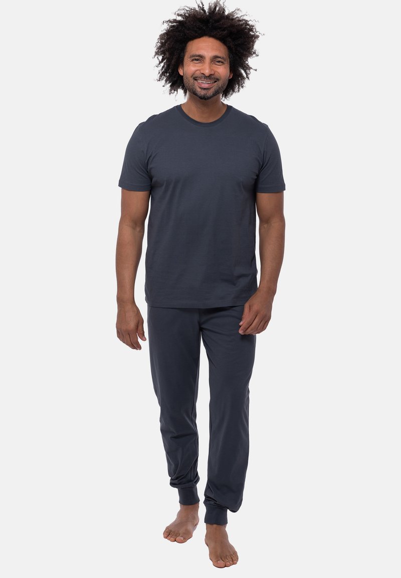 Czarny, szary t-shirt z krótkimi rękawami w połączeniu z dopasowanymi spodniami dresowymi. Spodnie mają elastyczne mankiety i luźny krój. Bez obuwia.