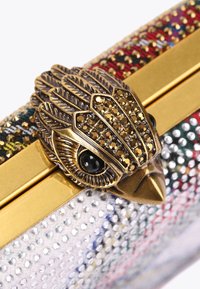 Metaliczna kopertówka z ciałem ozdobionym wielokolorowymi ćwiekami. Oferuje zapięcie w kształcie złotego orła z akcentami w postaci kamieni oraz gładką powierzchnię.