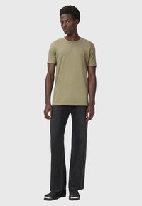 T-shirt in cotone verde oliva con maniche corte e collo rotondo, abbinato a jeans neri a gamba larga e stivali neri con dettagli bianchi.