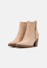 Beige suede ankle boots with a pointed toe, side zipper, and a stacked heel for stability. Smooth texture with minimal detailing.