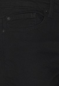 Jeans in denim nero con una texture sottile, dotati di una tasca frontale e un bottone in metallo. I dettagli delle cuciture sono visibili lungo i bordi.