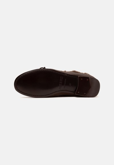 Semelle d'une chaussure en cuir marron montrée à plat avec des coutures visibles, nom de la marque et un talon rectangulaire avec quatre clous.