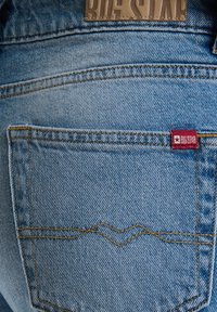 Jeans de mezclilla azul con un parche de cuero Big Star, costuras doradas y una pequeña etiqueta roja en el bolsillo trasero. Diseño clásico de 5 bolsillos.