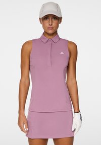 Ärmlös golfpolo och kjolset i ljusrosa, med krage, elegant design och diskret logotyp på bröstet.