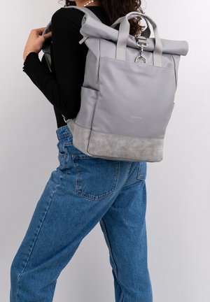 Sac à dos gris avec un fond texturé gris, des bretelles ajustables et une poche avant. Il est fabriqué en un matériau lisse.
