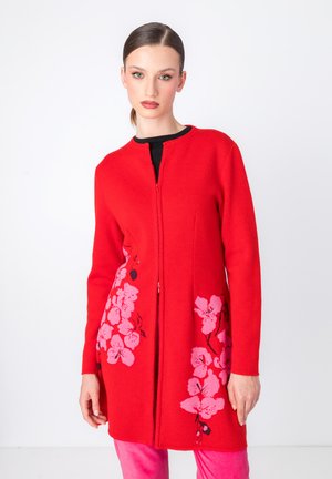 Rode gebreide cardigan met een ritssluiting aan de voorkant, voorzien van roze bloem borduursels aan de zijkanten. Lange mouwen en ronde halslijn.