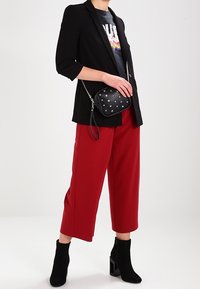 Černý blazer přes grafické tričko, červené široké kalhoty a černé kotníkové boty. Malá černá kabelka s stříbrnými hroty.