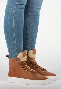 Ruske suede visoke patike s mekanim kremastim postavom, bež pertlama i belim gumiranim đonom; prikazane sa plavim uskim farmerkama.