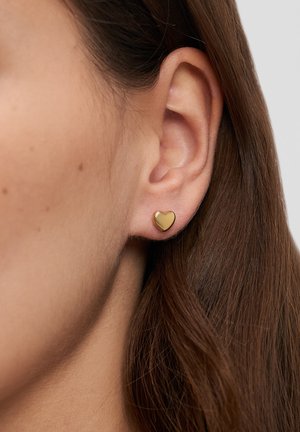 Gold-toned heart-shaped stud earring, smooth finish, attached to a pierced earlobe, featuring a polished surface and rounded edges.