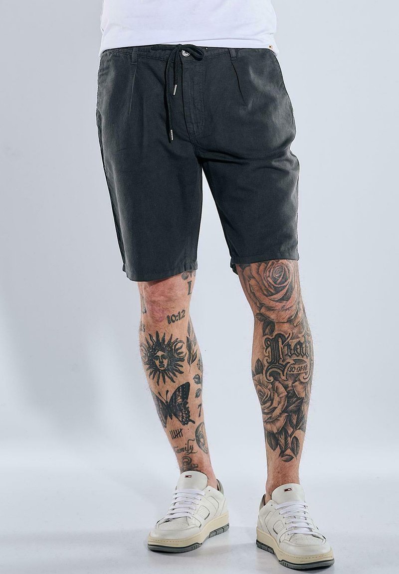 Dark grey shorts with a drawstring waist, featuring a relaxed fit and subtle texture, paired with white sneakers.