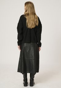 Schwarzer Strickpullover mit lockerer Passform, kombiniert mit einem langen schwarzen Lederrock. Kniehohe Stiefel vervollständigen den monochromen Look.