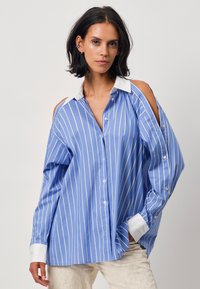 Blue and white striped button-up shirt with cold shoulder design, collar, and long sleeves. Made of lightweight fabric, relaxed fit.